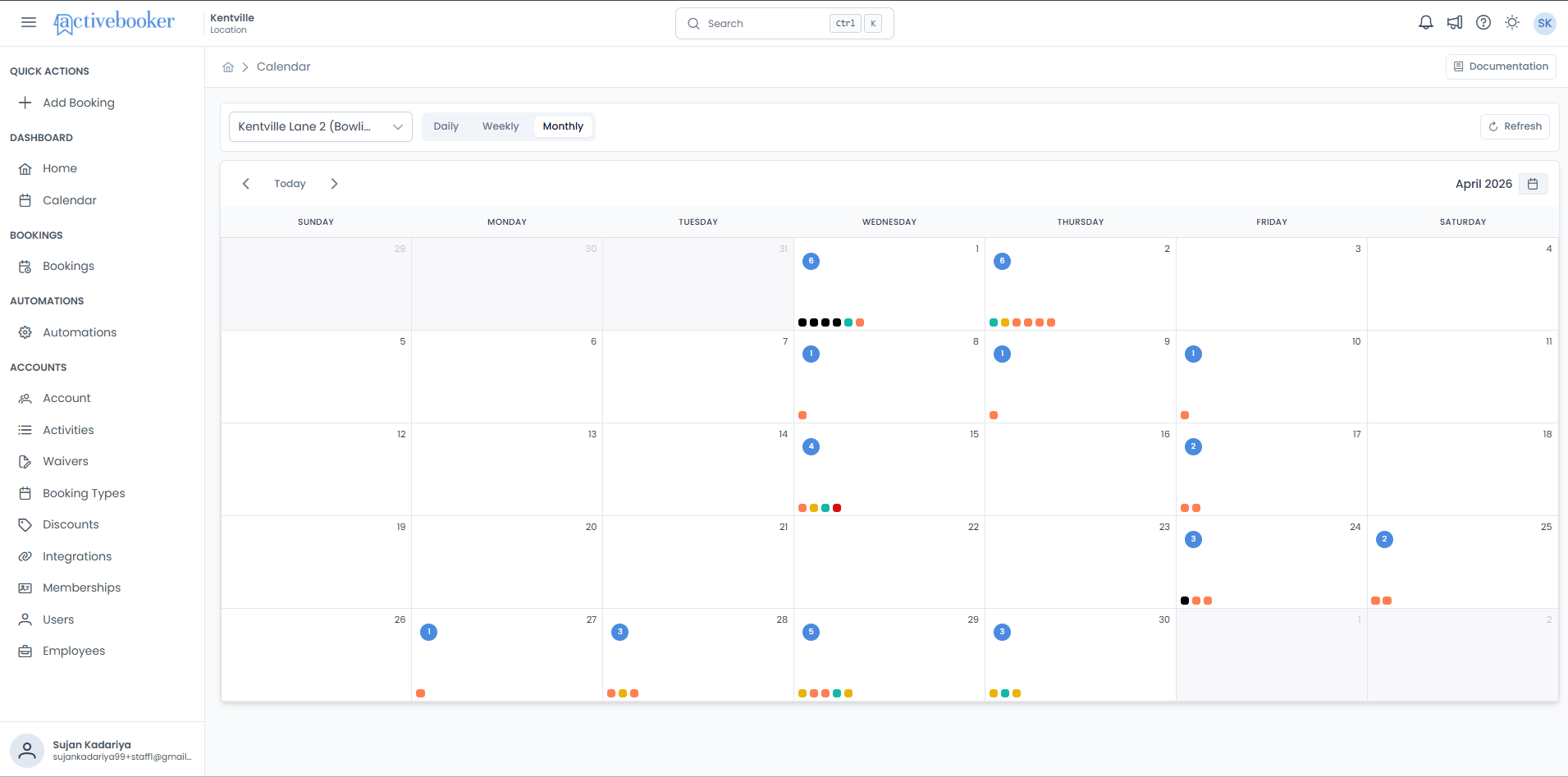Monthly calendar view showing a full month grid with blue booking-count badges and colour dots on each active day
